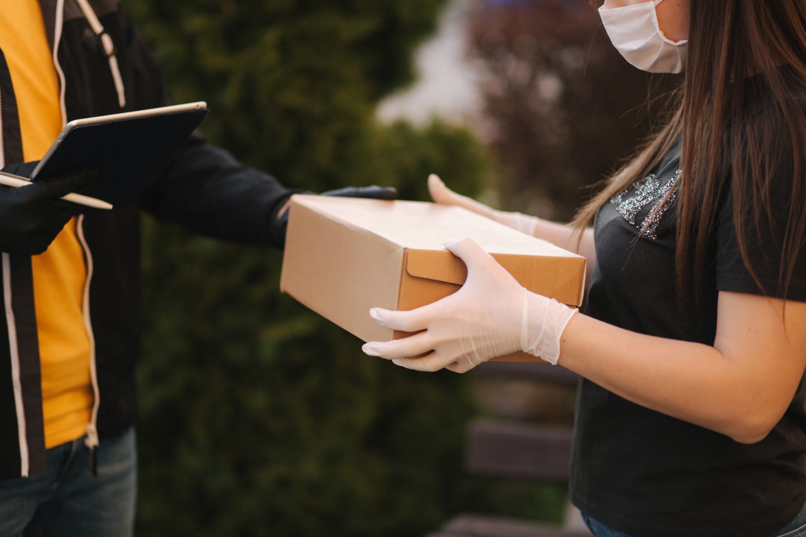 Man from delivery service in mask and gloves handing over parcel