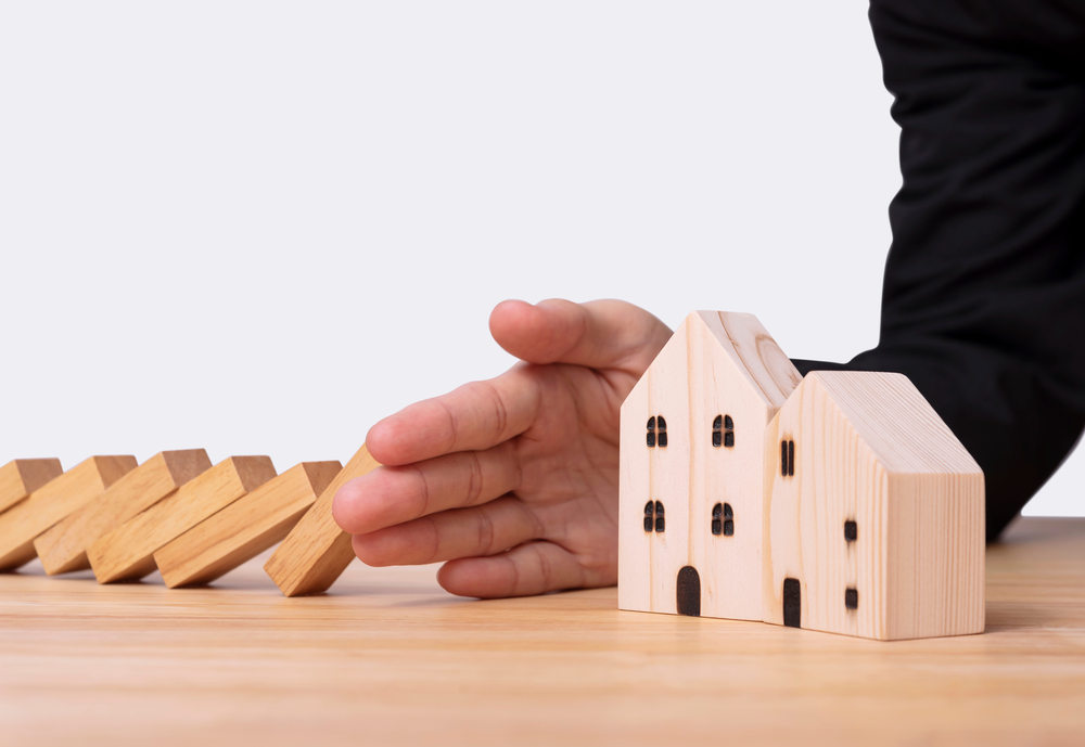 Hand stopping dominoes hit wooden home.