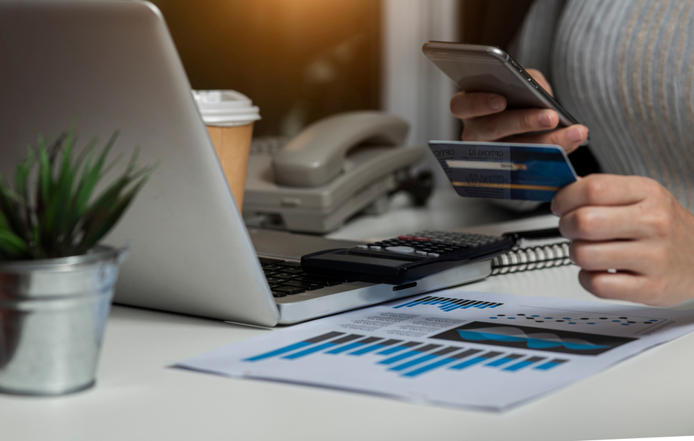 Person holding credit card and using smartphone with laptop computer.