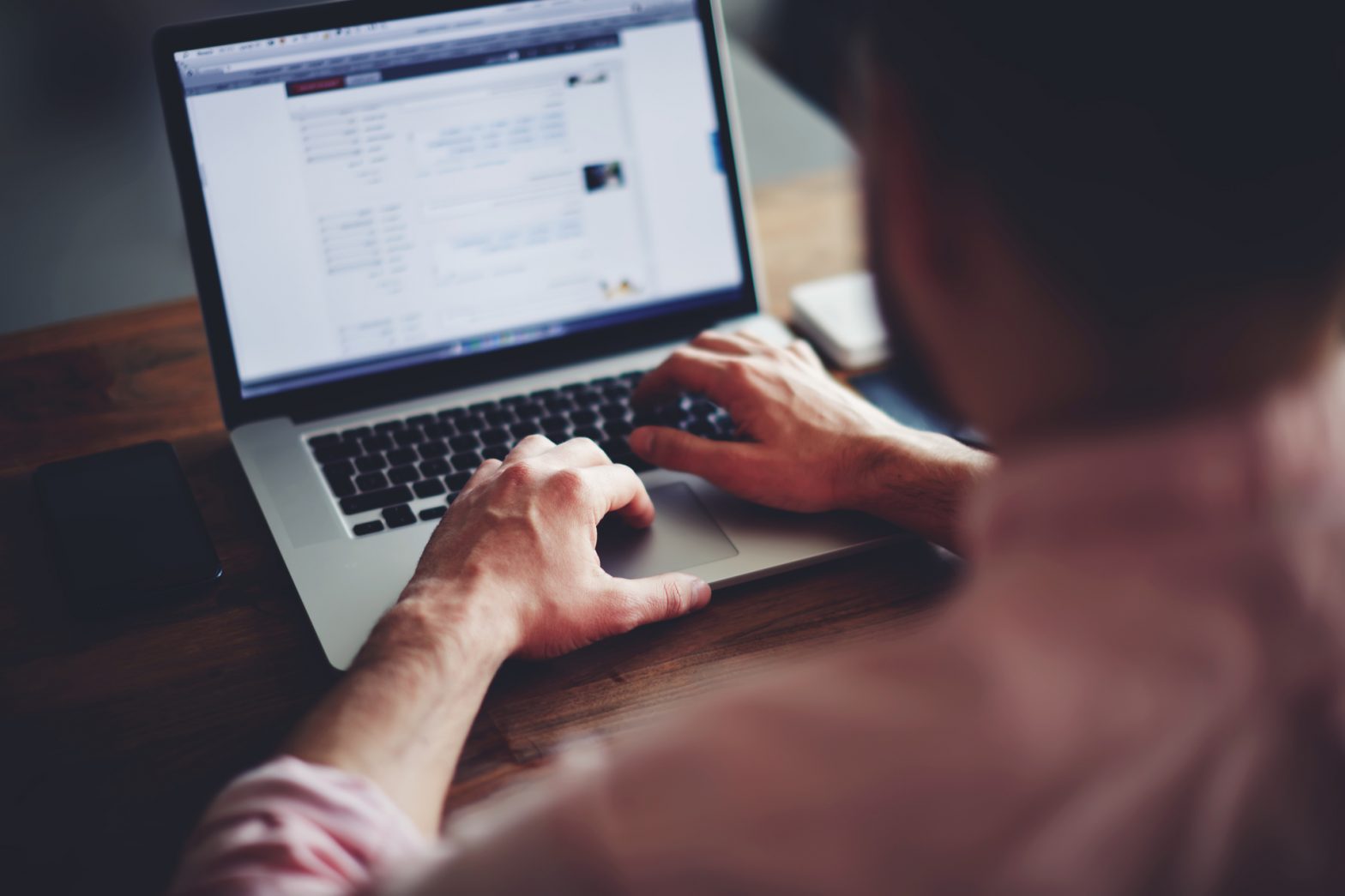 Image of a man, upi can't see his face, but he is typing on his laptop
