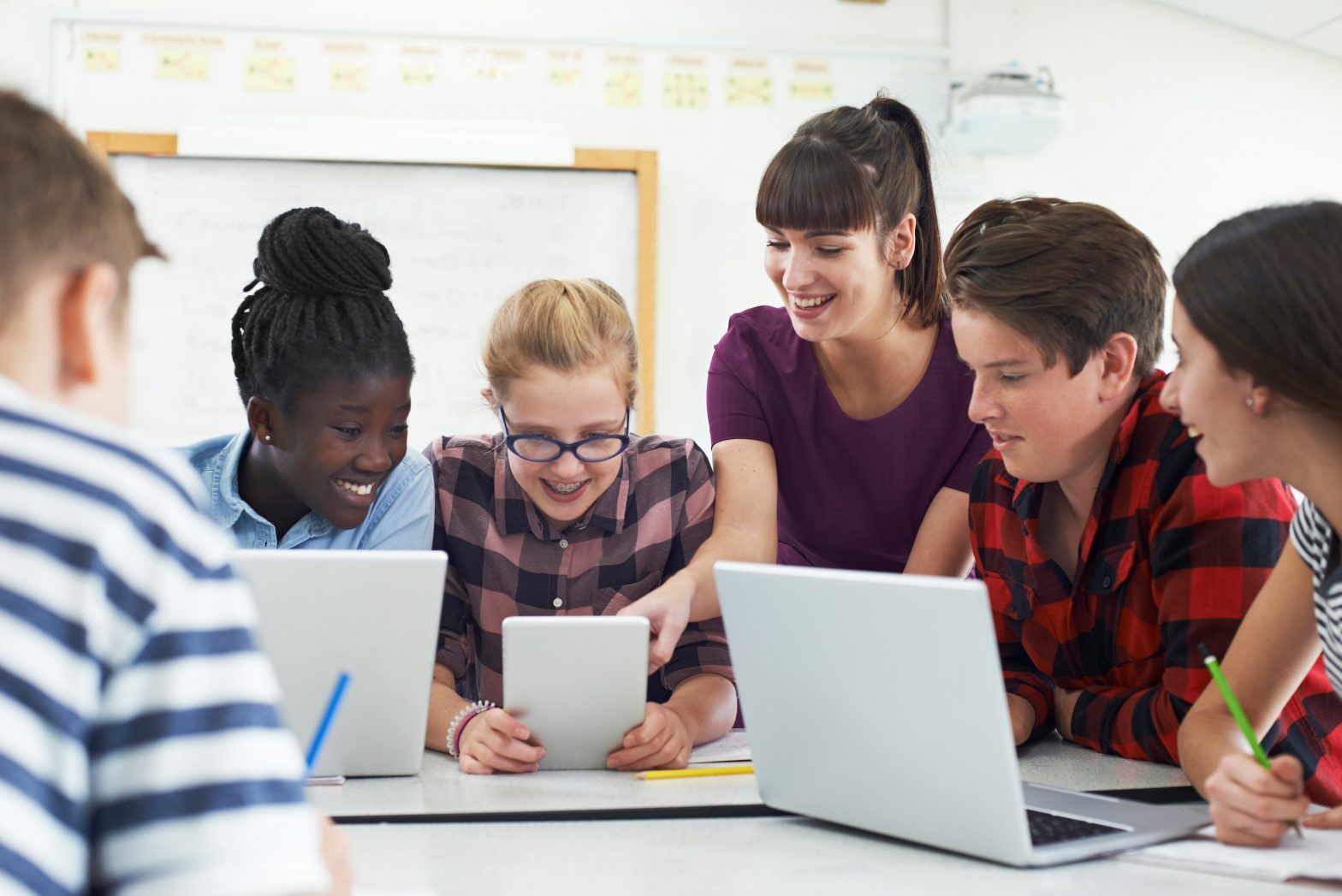 Group of children and teacher looking at laptops and a tablet
