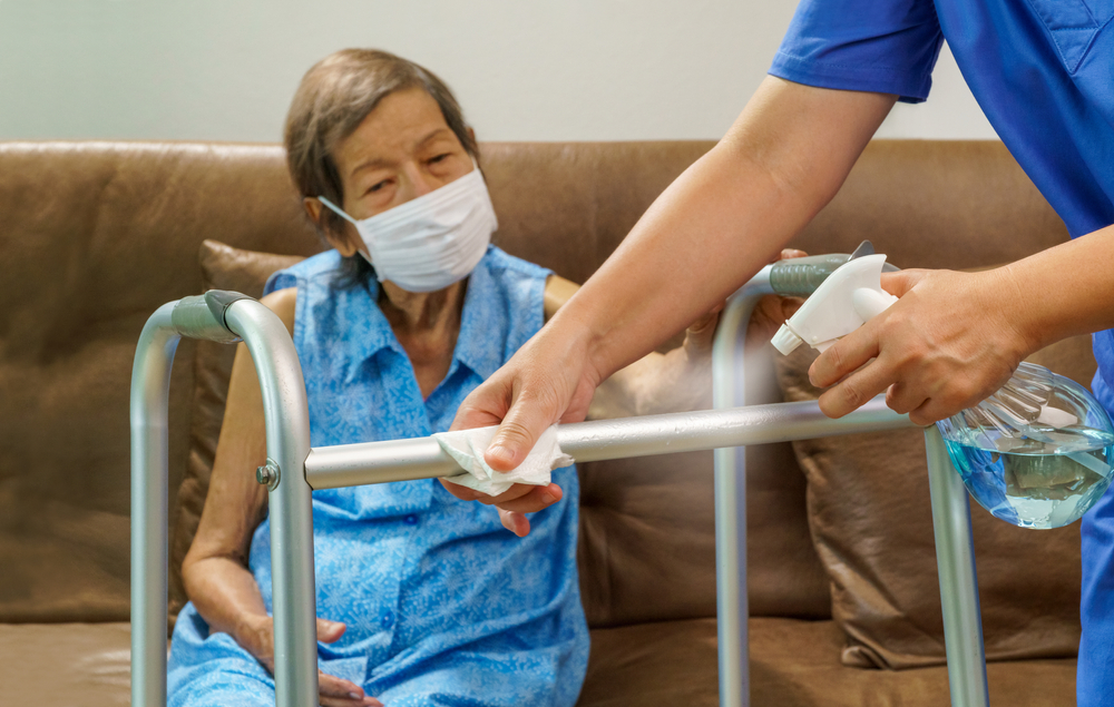 Elderly female care home resident sitting on sofa, with hands in shot of walking frame being cleaned
